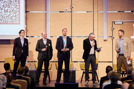 Mehrere Personen stehen auf der Bühne mit Mikrofonen und präsentieren Ergebnisse aus Workshops vor dem Publikum.