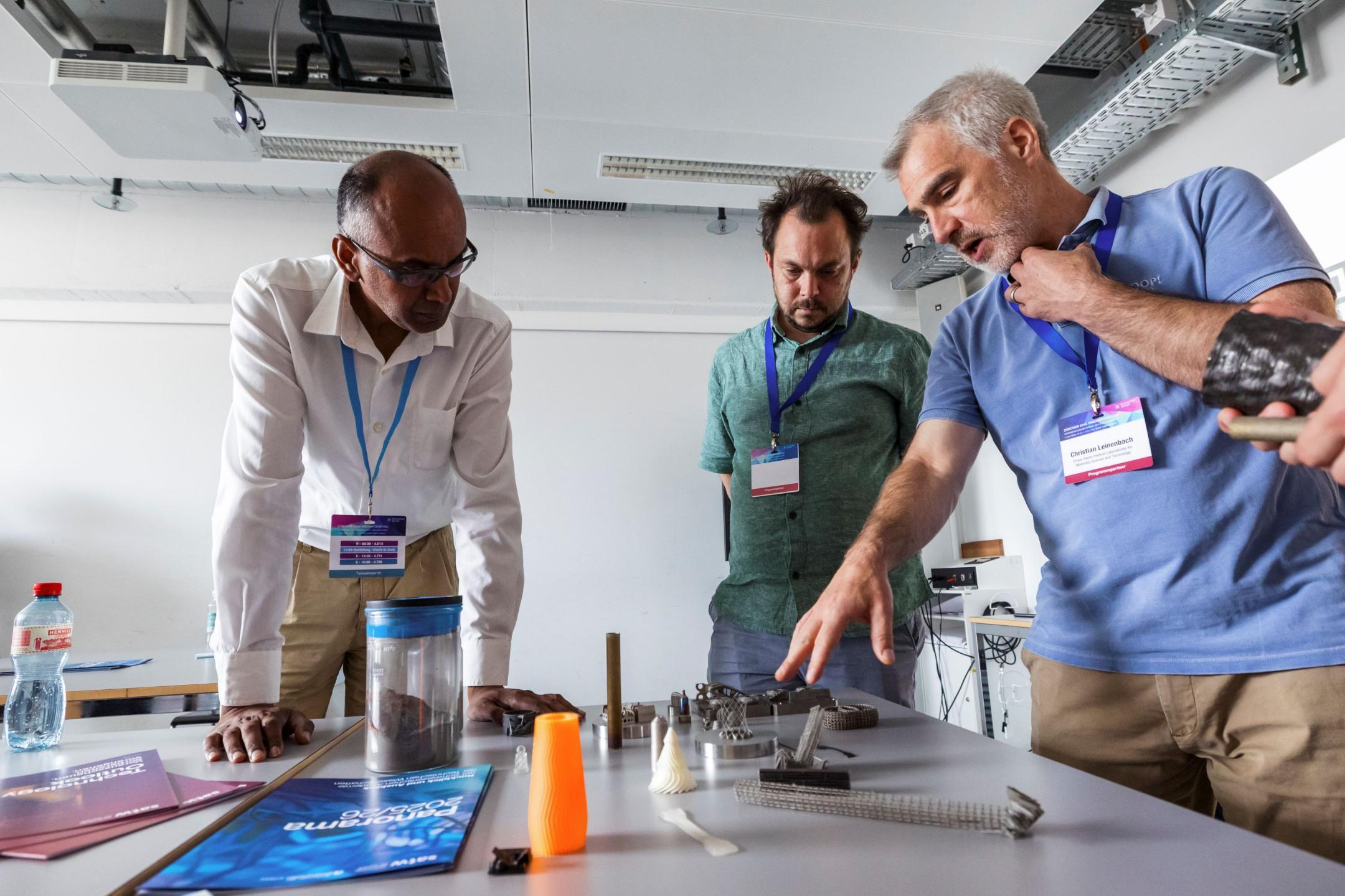 Drei Workshopteilnehmende stehen um einen Tisch mit 3D-Drucker-Produkten und diskutieren über diese
