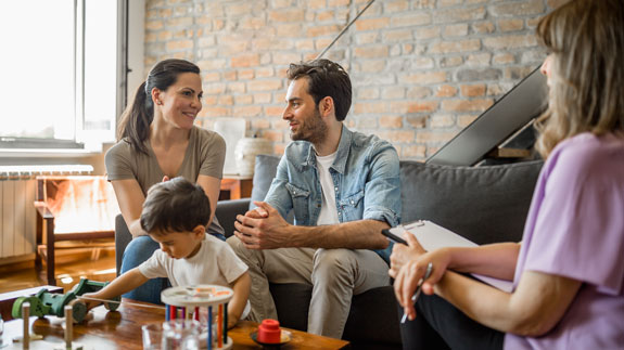 Eine Familie sitzt gemeinsam im Wohnzimmer mit einer Fachperson