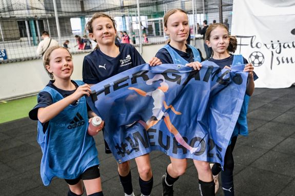 Vier junge Fussballerinnen halten ein blaues Banner mit einer Illustration einer Spielerin und den Worten &laquo;HERGAME&raquo; und &laquo;#WEURO2022&raquo;.