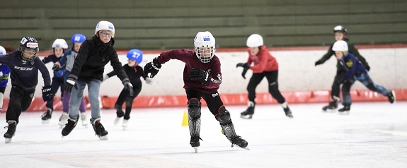 Kinder mit Schlittschuhen und Helm auf dem Eis