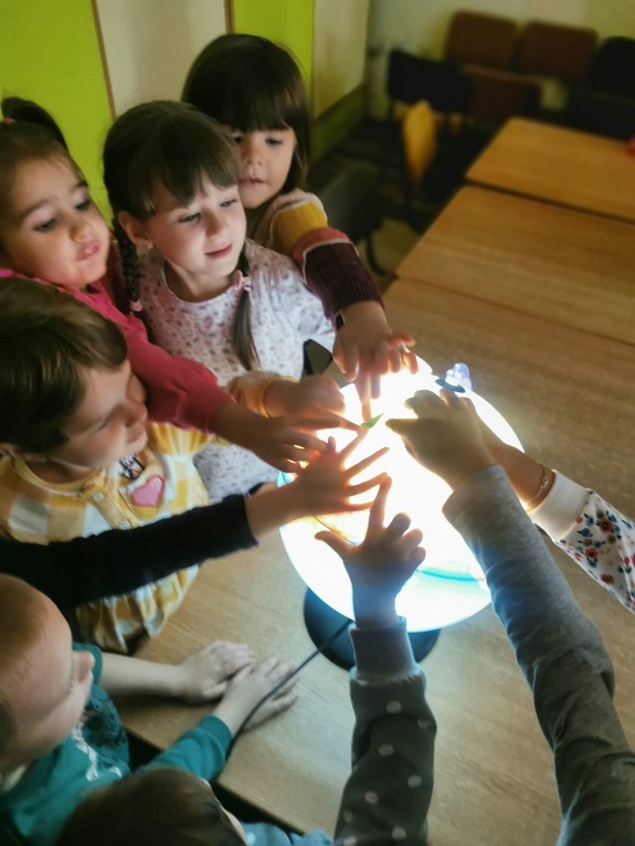 Kinder halten ihre Hände auf eine beleuchtete Weltkugel