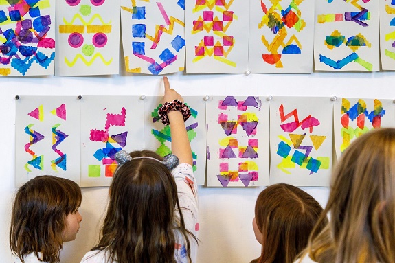 Kinder stehen vor Bildern, die vermutlich mit Stempeln gemacht wurden
