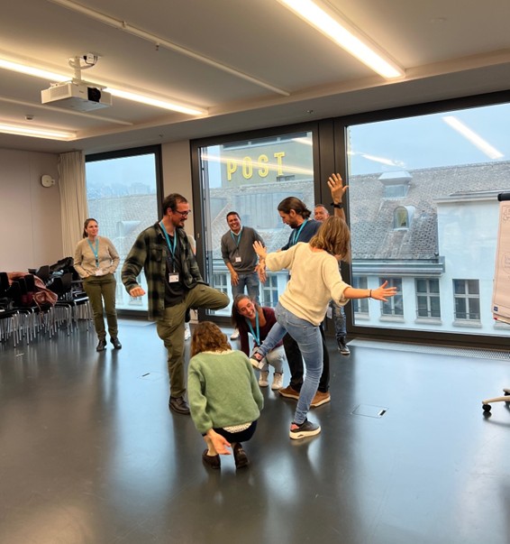 Mehrere Personen stehen in einem hellen Raum und machen eine gemeinsame Bewegungs- oder Gruppenspiel-&Uuml;bung