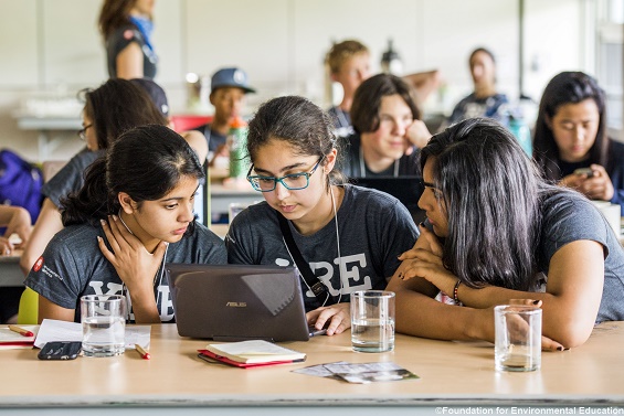 Ein Klassenzimmer: Drei Sch&uuml;lerinnen betrachten etwas auf einem Tablet.