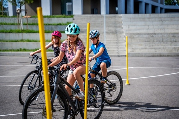 Drei Sch&uuml;lerinnen und Sch&uuml;ler fahren mit dem Velo einen Parcours