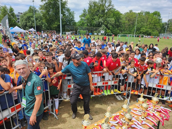 Grosser Andrang von Kindern und Jugendlichen bei einem Fussballturnier mit Pokalen im Vordergrund.