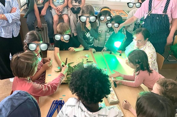 Kinder sitzen um einen Tisch und untersuchen gemeinsam Gegenst&auml;nde mit Lupen.