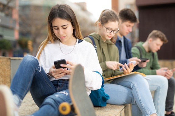 Vier Jugendliche sitzen nebeneinander und schauen jeweils auf ihr Smartphone.