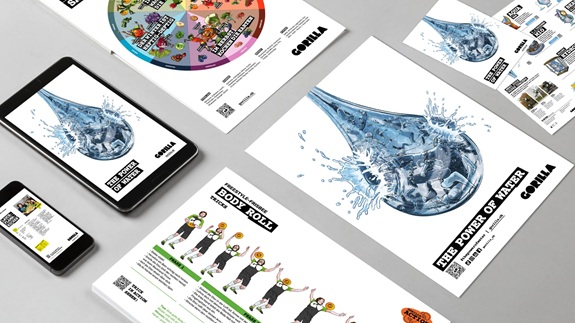 Mehrere Werbematerialien mit dem Motiv eines grossen, spritzenden Wassertropfens sowie Illustrationen und Infografiken liegen auf einem Tisch, darunter Flyer, Poster und digitale Ansichten auf Smartphone und Tablet.