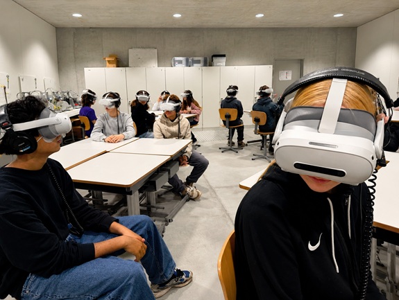 Sch&uuml;lerinnen und Sch&uuml;ler sitzen mit VR‑Brillen an Tischen in einem Klassenzimmer.