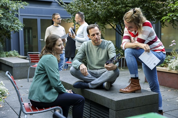 Erwachsene sitzen und stehen im Freien zusammen und besprechen Unterlagen.