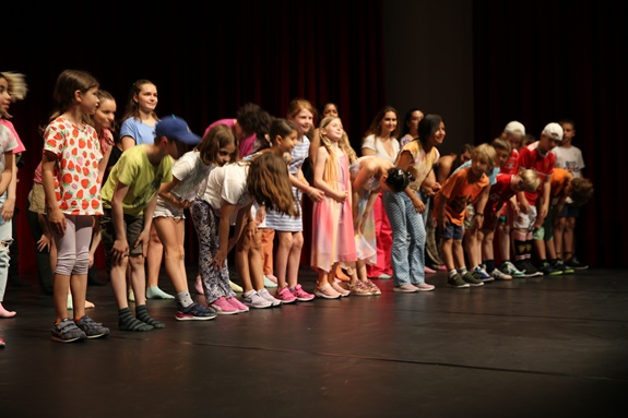 Eine Gruppe von Kindern steht auf einer Theaterb&uuml;hne und verbeugt sich gemeinsam nach einer Auff&uuml;hrung.