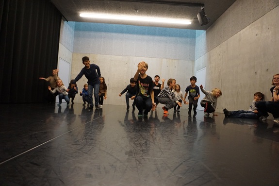 Gruppe von Kindern bewegt sich gemeinsam tanzend in einem leeren Raum.