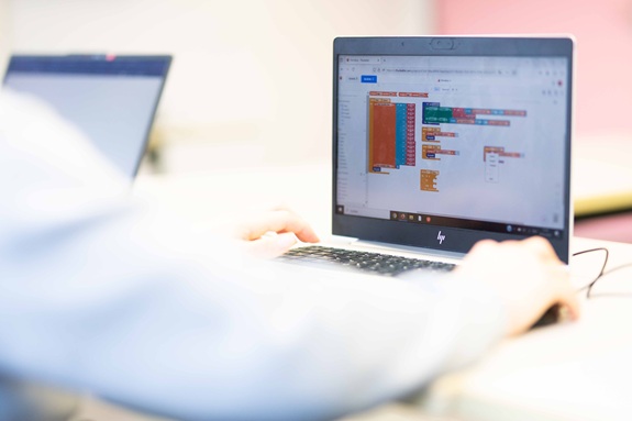 Person arbeitet an einem Laptop, auf dem eine visuelle Programmieroberfl&auml;che mit bunten Code-Bl&ouml;cken zu sehen ist.