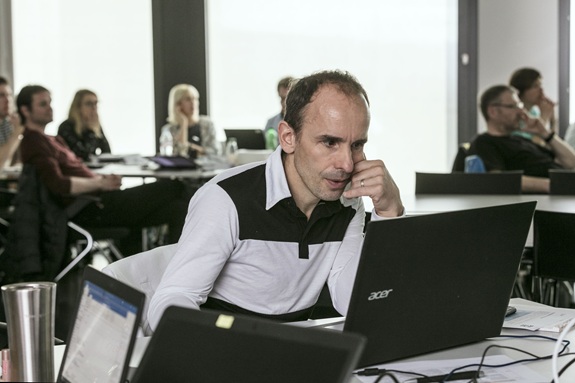 Personen sitzen in einem Seminarraum an Tischen mit Laptops, im Vordergrund eine Person konzentriert vor einem Bildschirm.
