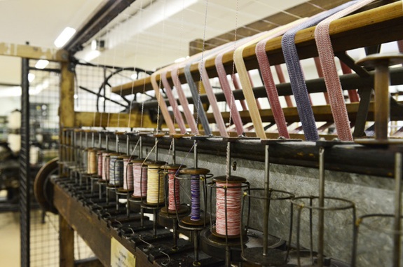 Eine industrielle Maschine mit aufgereihten Garnspulen in einer Fabrikhalle.