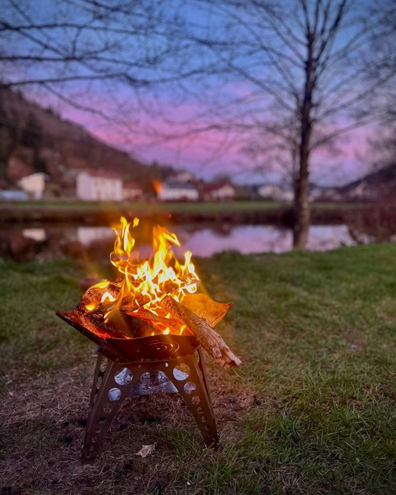 Ein kleines Feuer brennt in einer Feuerschale im Freien bei Abendd&auml;mmerung.  