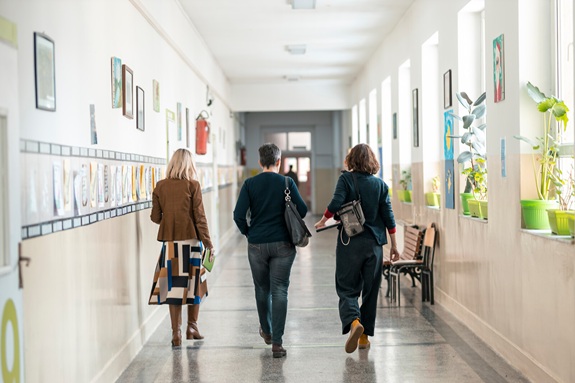 Drei Personen gehen durch den Korridor eines Schulgeb&auml;udes.