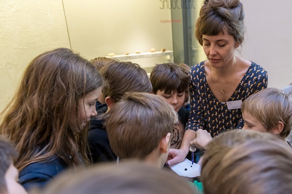 Eine Gruppe von Kindern sammelt sich um eine Ausstellungsführerin