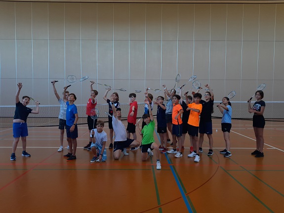 Kinder in Sportkleidern strecken ihren Badmintonschläger in die Luft