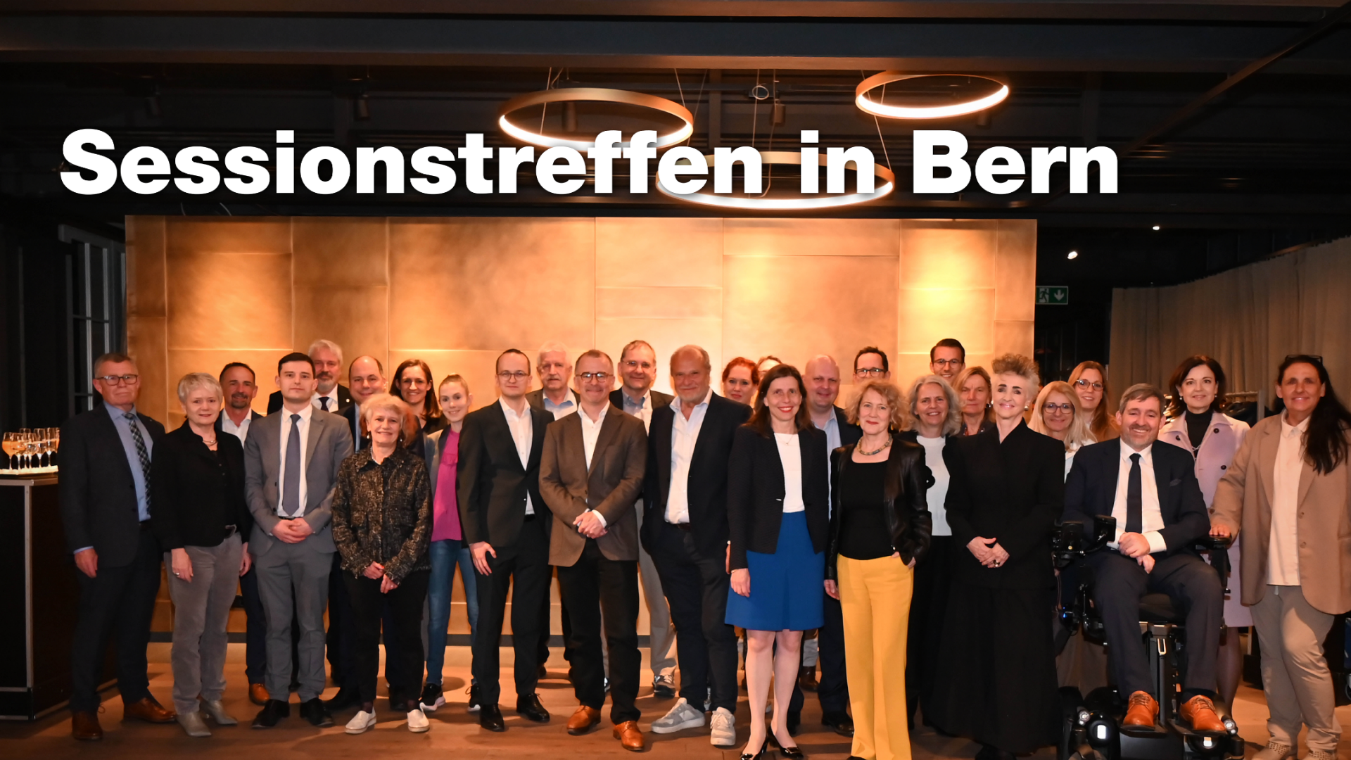 Gruppe von 30 Männern und Frauen, meist in Businesskleidung, stehen und lächeln. Ein Mann sitzt im Rollstuhl. Auf dem Bild steht «Sessionstreffen in Bern».