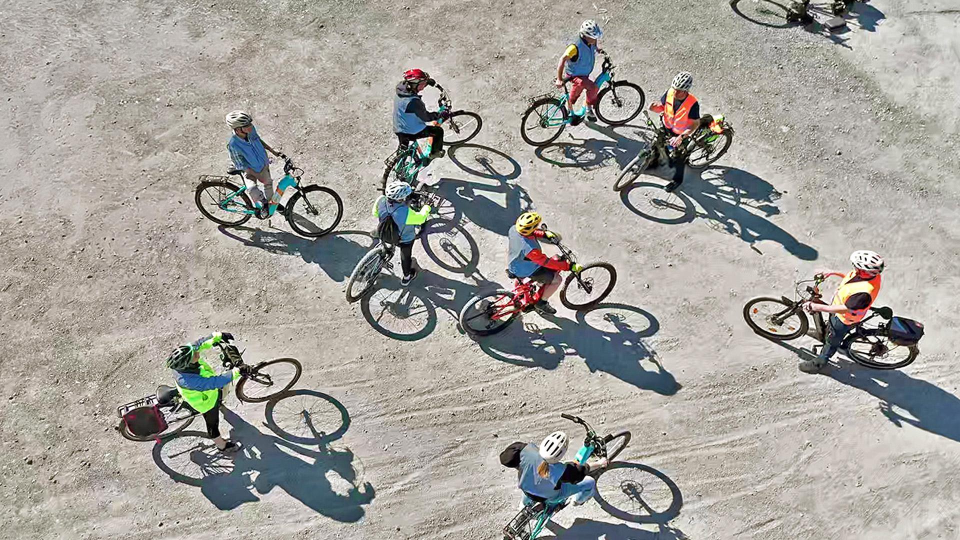 Luftbild: Mehrere Velofahrende üben auf einem grossen Platz ausserhalb des Verkehrs das Bremsen. 