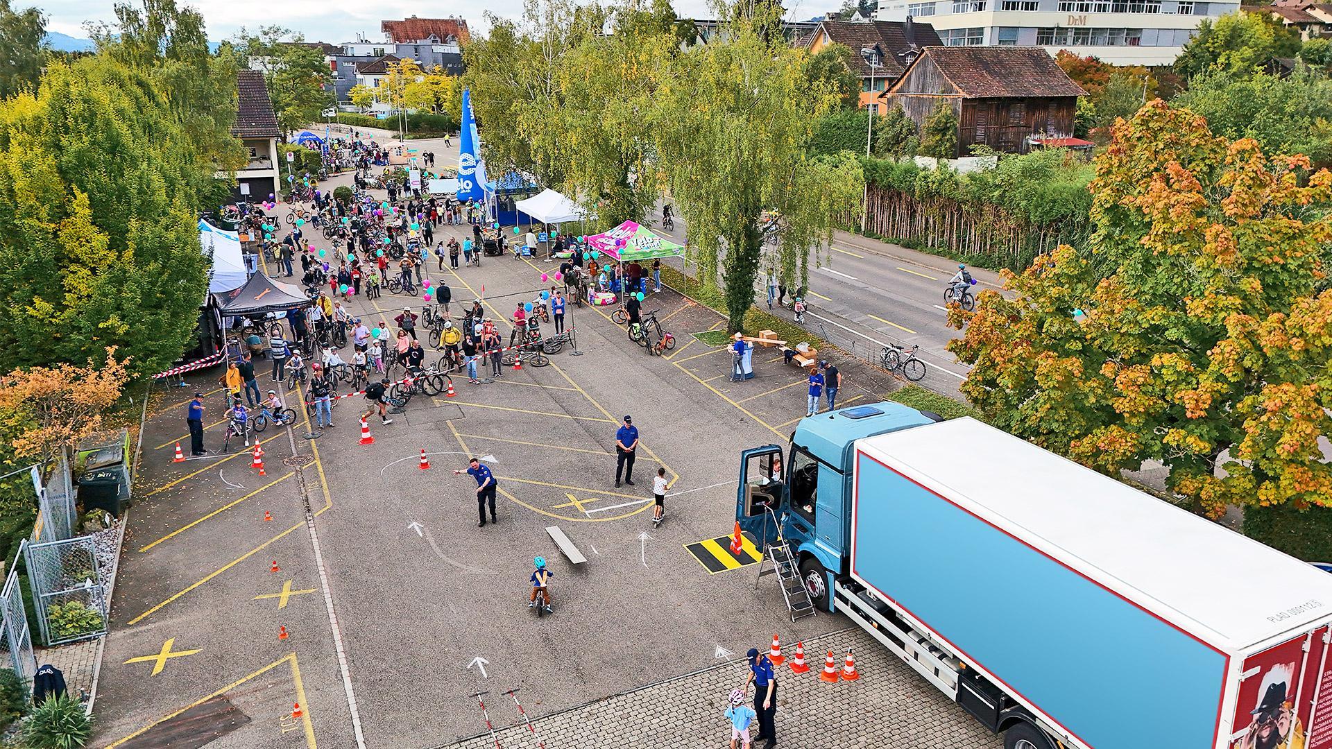 Belebter Parkplatz mit Slow-Up-Besuchern Velos und einem Kinderparcours. Ein der LKW mit geöffneter Kabinentür parkiert für das Erleben der Sicht aus einer Fahrkabine.