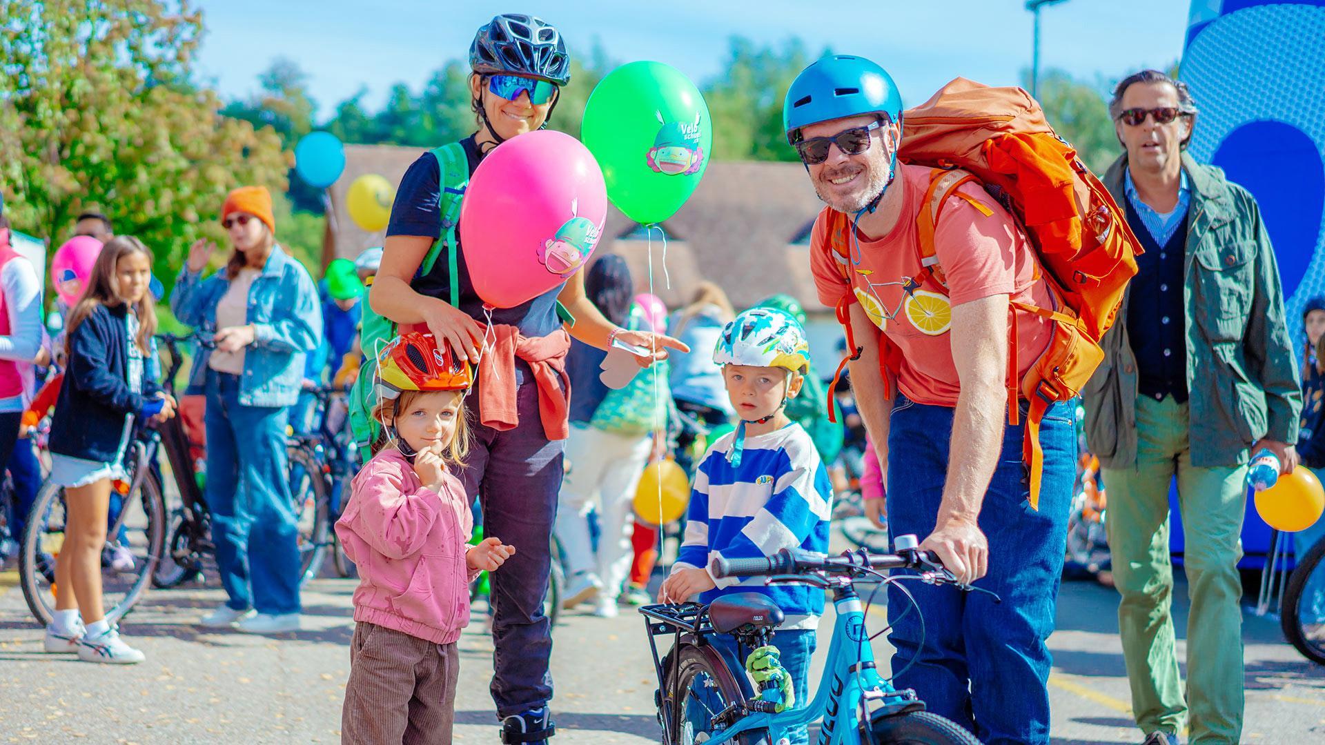 Eine Familie beim Slowup Zürichsee: Mutter, Vater und zwei Kinder mit Fahrradhelmen und Ballons posieren lächelnd im Freien.